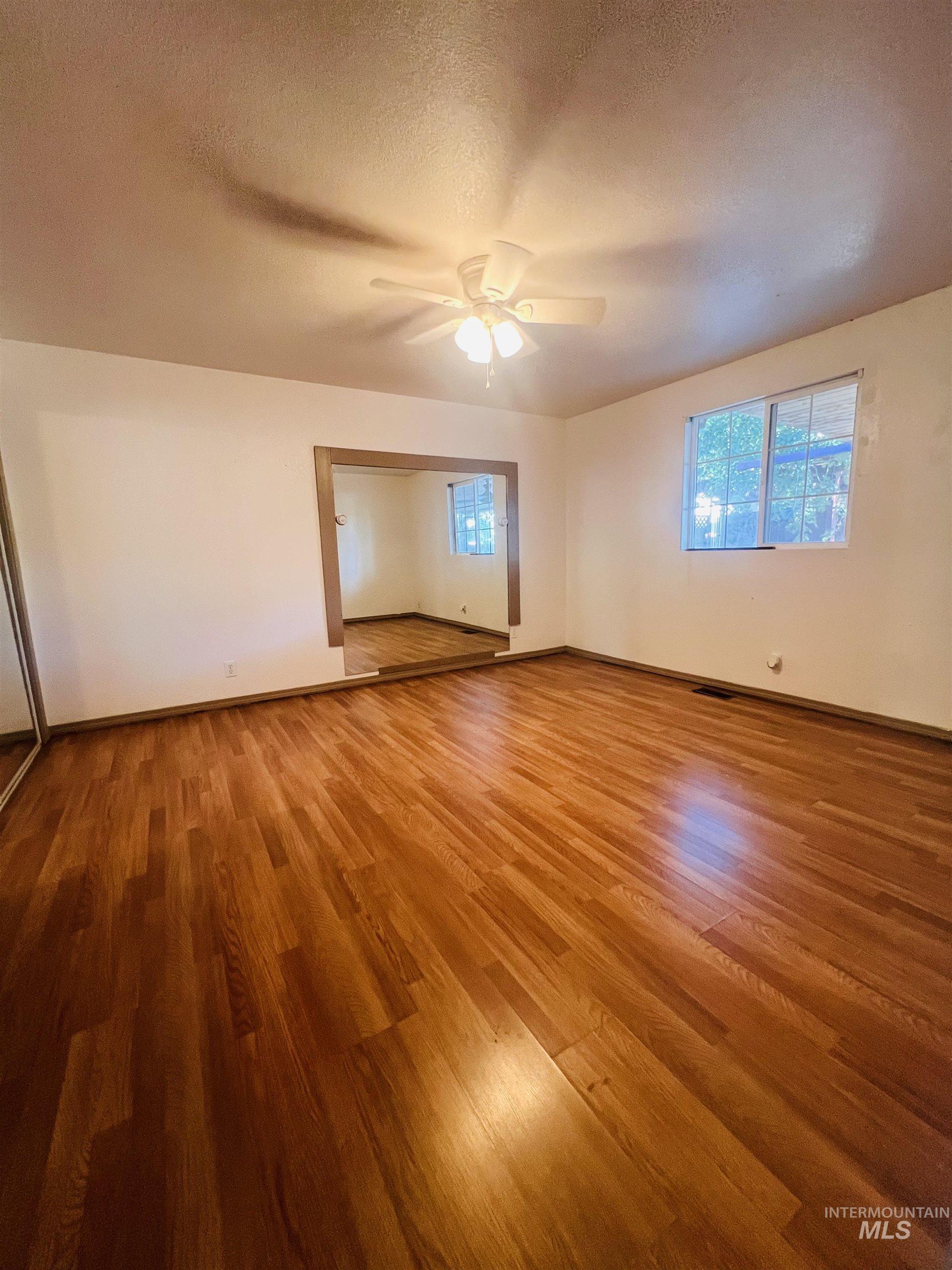 Spacious room featuring wood-finish flooring, a ceiling fan with integrated lighting, and a large window