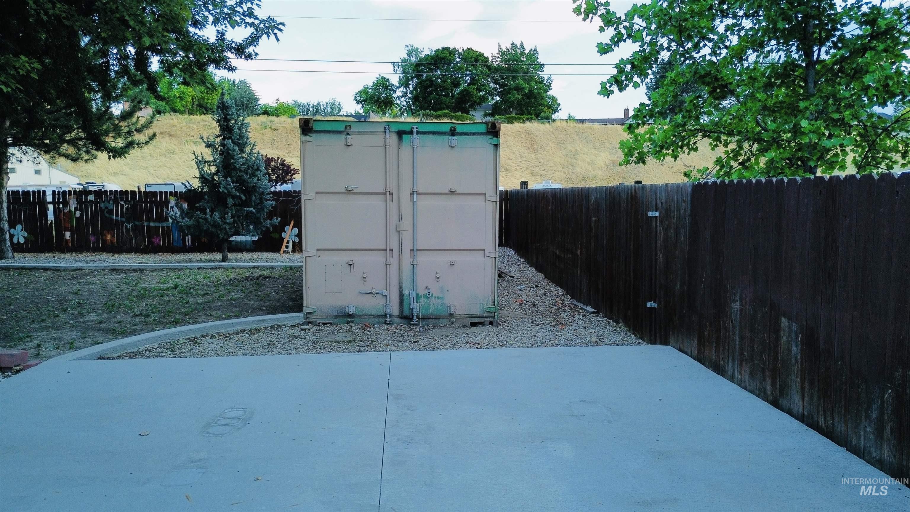 Concrete patio area with a privacy fence, gravel landscaping, and a storage container