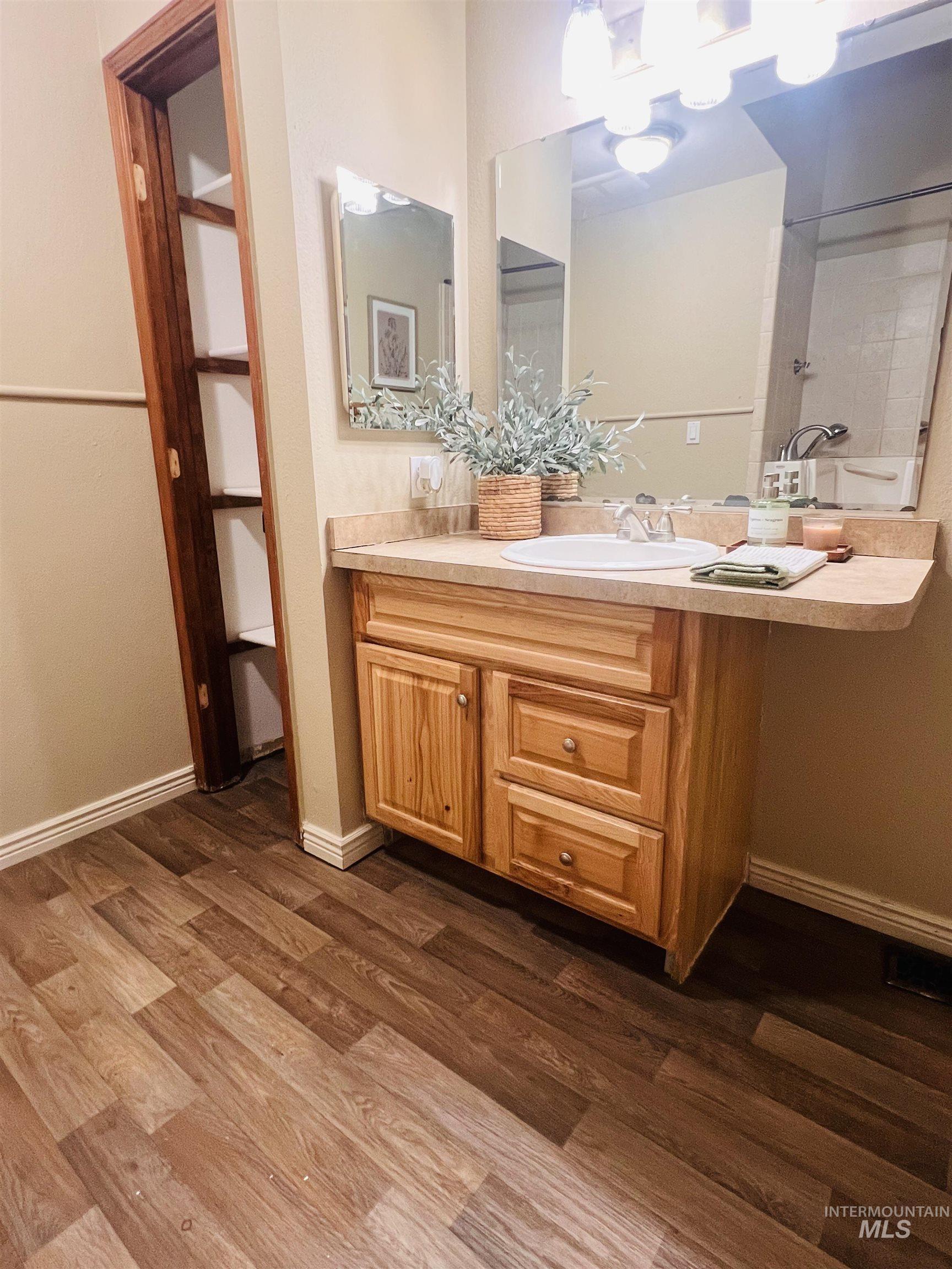 Bathroom featuring a wood-finish flooring, a vanity with a light-toned countertop, an integrated sink, and an overhead vanity light fixture
