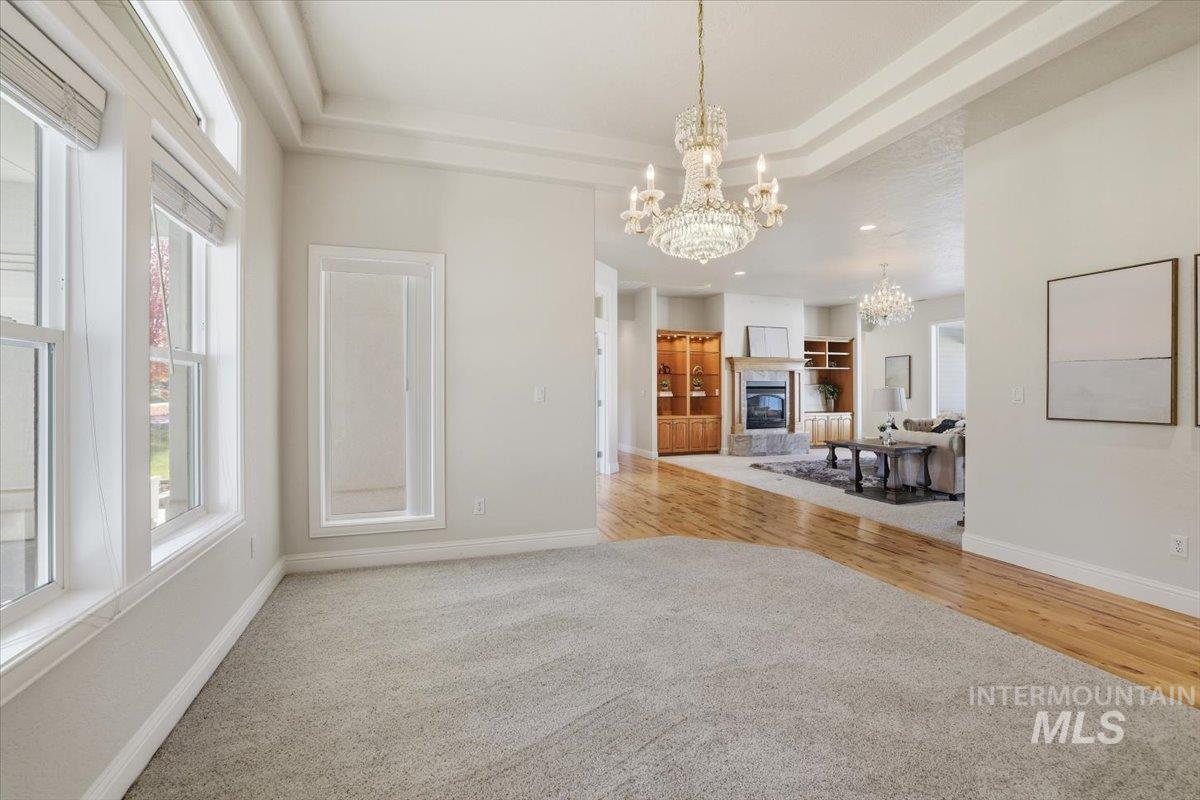 Dining area with a chandelier, a raised ceiling, a glass covered fireplace, light wood-style flooring, and light colored carpet