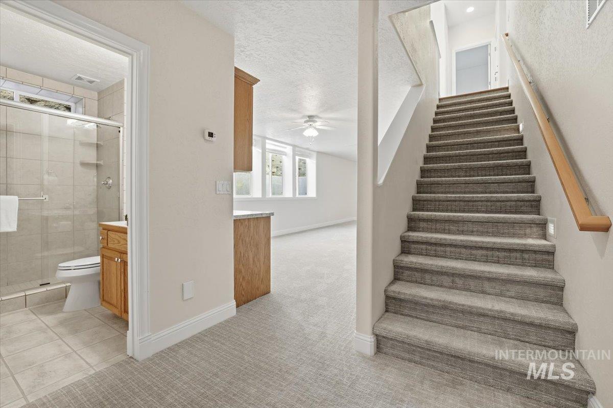 Stairs featuring carpet flooring, a textured ceiling, ceiling fan, and tile patterned floors