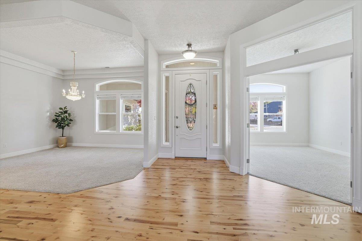 Entrance foyer with light carpet, light wood-type flooring, a chandelier, and a textured ceiling