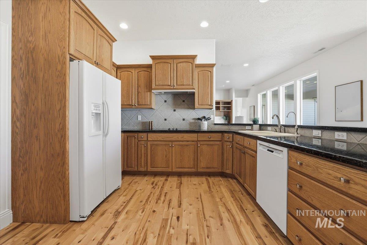 Kitchen featuring brown cabinetry, backsplash, white appliances, light wood-type flooring, and recessed lighting