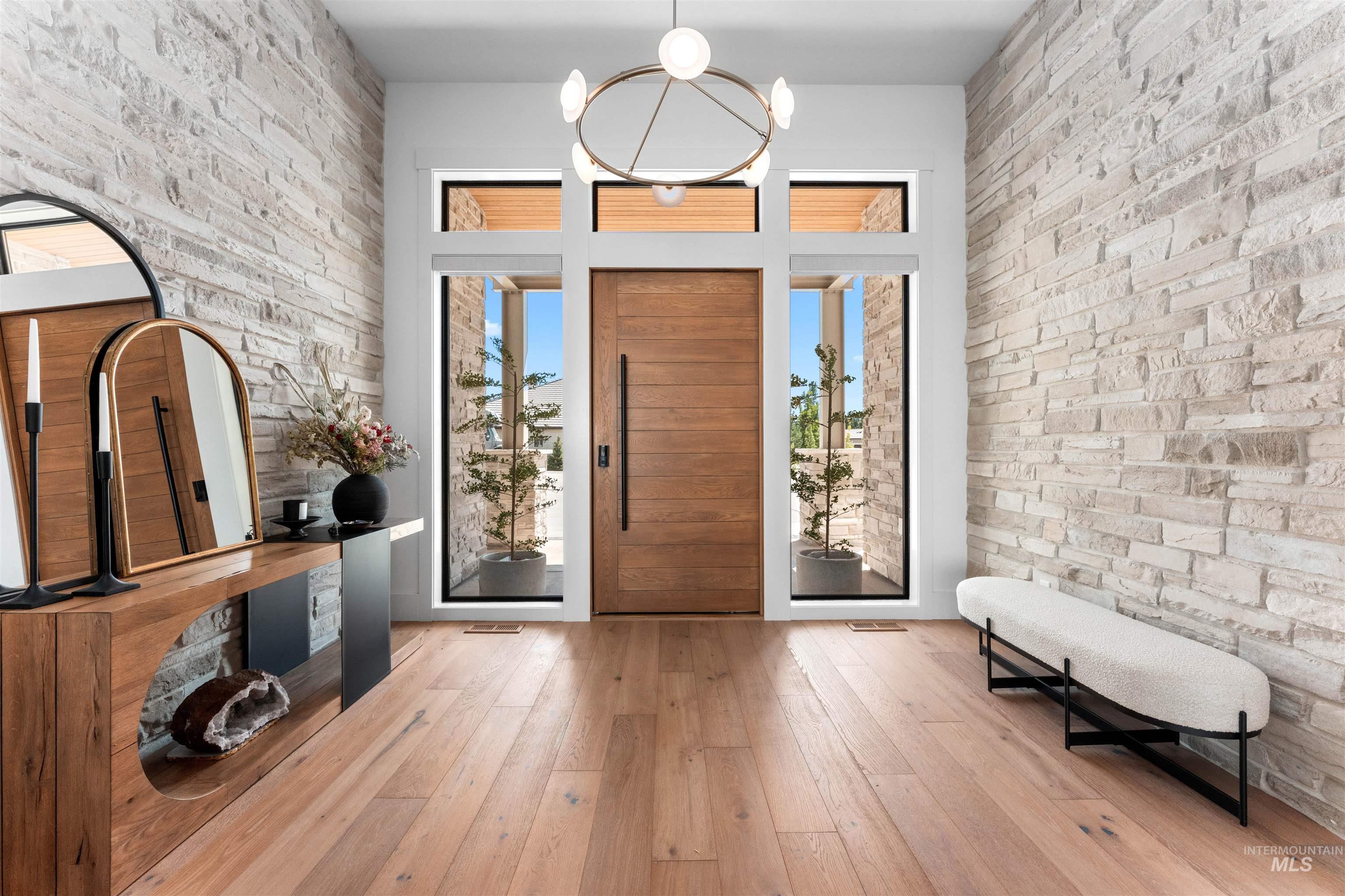 Entrance foyer with wood-type flooring, brick wall, and a chandelier