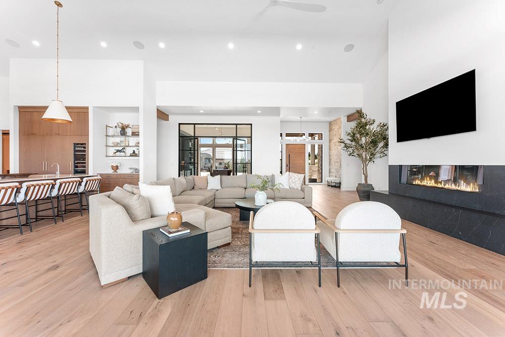 Living room with light wood finished floors, a glass covered fireplace, recessed lighting, and a high ceiling
