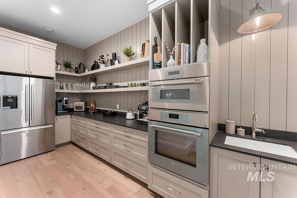 Kitchen with appliances with stainless steel finishes, dark countertops, light wood-style floors, and open shelves