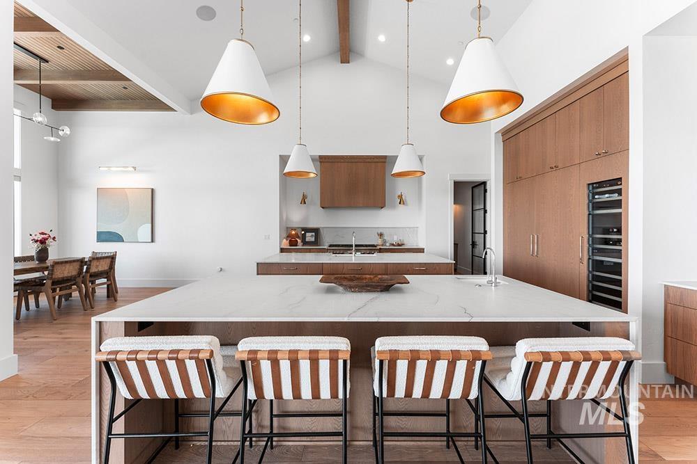 Kitchen featuring light wood-style flooring, beam ceiling, high vaulted ceiling, a large island with sink, and modern cabinets