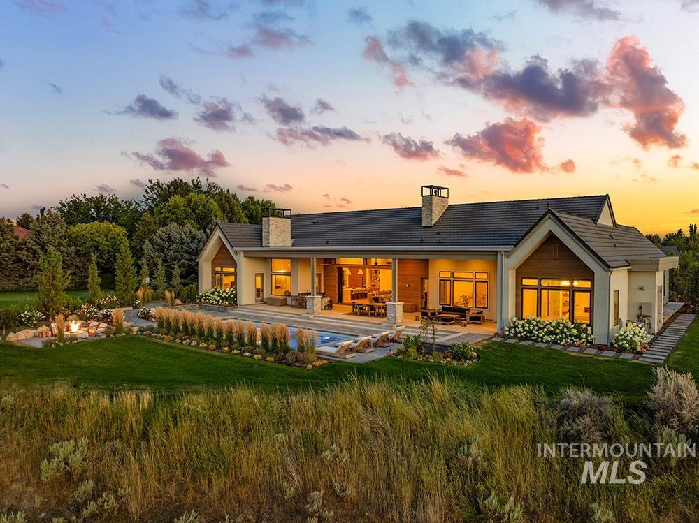 Back of house at dusk featuring a chimney, a yard, a patio area, and an outdoor pool