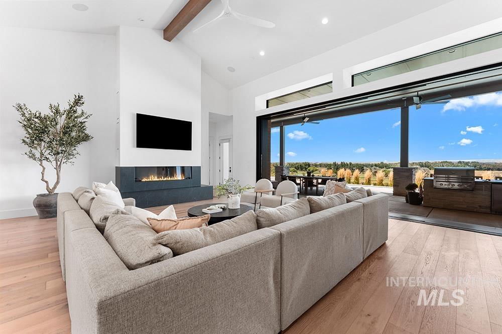 Living room with beamed ceiling, high vaulted ceiling, hardwood / wood-style flooring, a glass covered fireplace, and ceiling fan