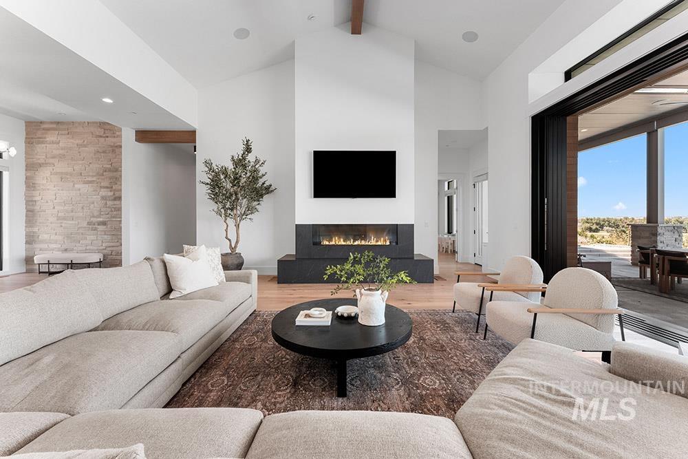 Living area featuring beam ceiling, a glass covered fireplace, high vaulted ceiling, and light wood finished floors