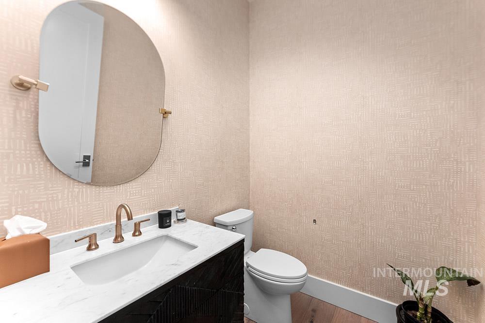 Half bathroom with wallpapered walls, vanity, and wood finished floors