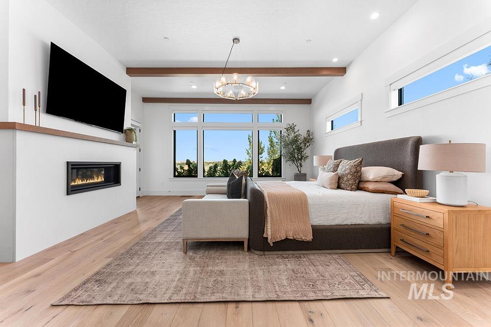 Bedroom with beamed ceiling, a glass covered fireplace, wood finished floors, recessed lighting, and a chandelier