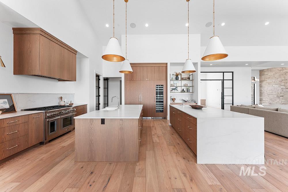 Kitchen featuring modern cabinets, open shelves, double oven range, a center island with sink, and light wood-type flooring