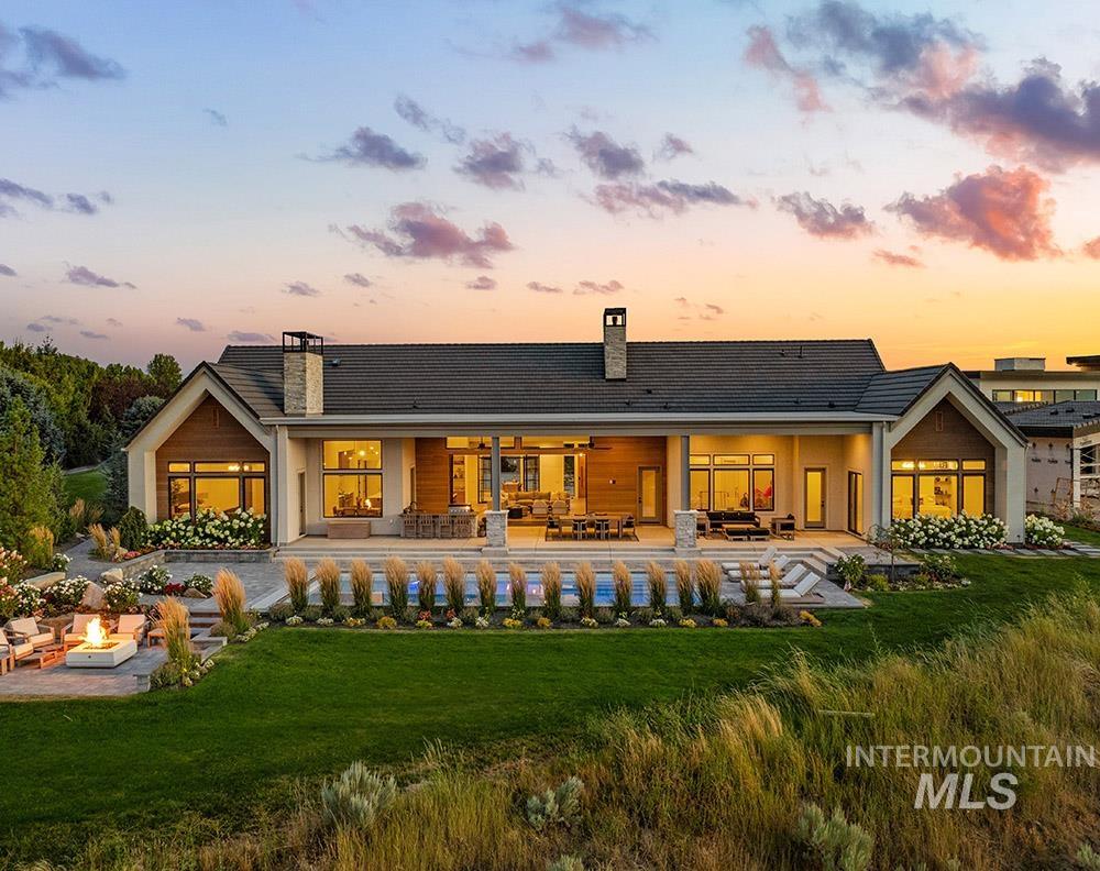 Back of house at dusk with an outdoor living space with a fire pit, a patio area, a chimney, a yard, and a ceiling fan