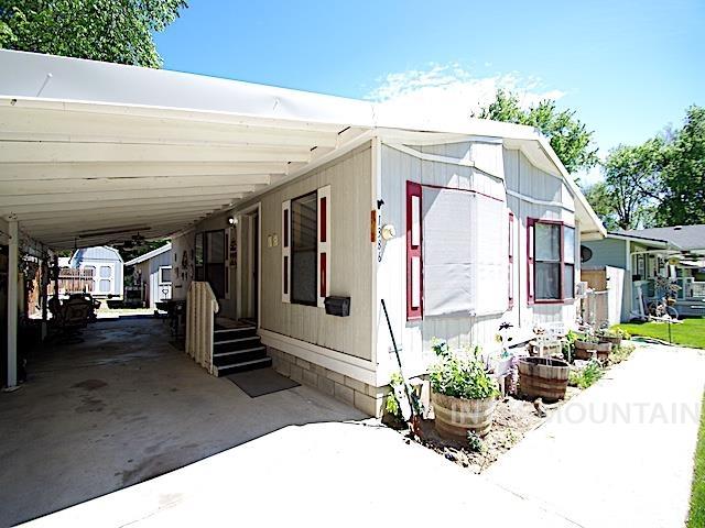 Exterior featuring an attached carport, light-colored siding, contrasting red window shutters, and a concrete pathway