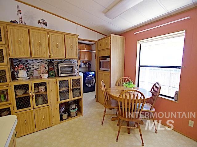 Eat-in kitchen featuring extensive wood-finish cabinetry, a patterned tile backsplash, a built-in microwave, and an adjacent utility area with a washing machine
