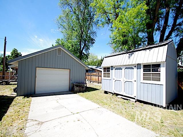 Detached garage with a white overhead door and an adjacent storage shed featuring double doors and side windows