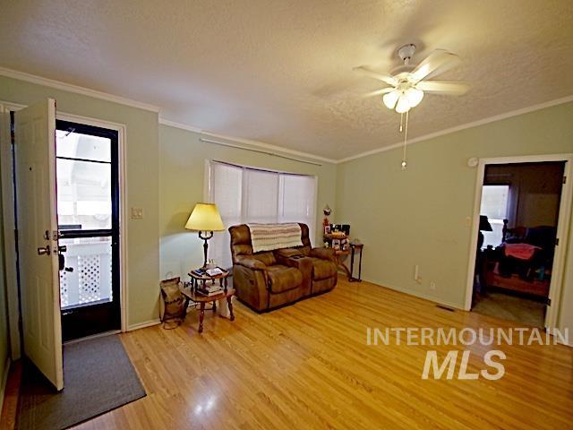 Living area featuring wood-finish flooring, light-toned wall paint, white crown molding, and a ceiling fan with integrated lighting