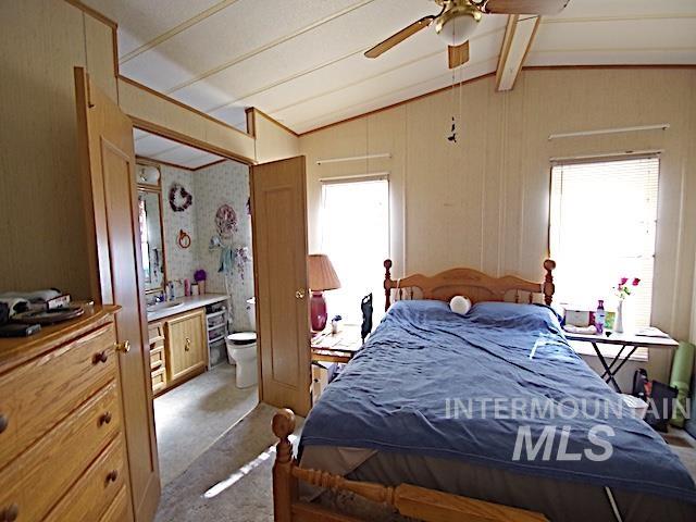 Bedroom featuring a ceiling fan with integrated lighting, wood-finish paneling, and two windows