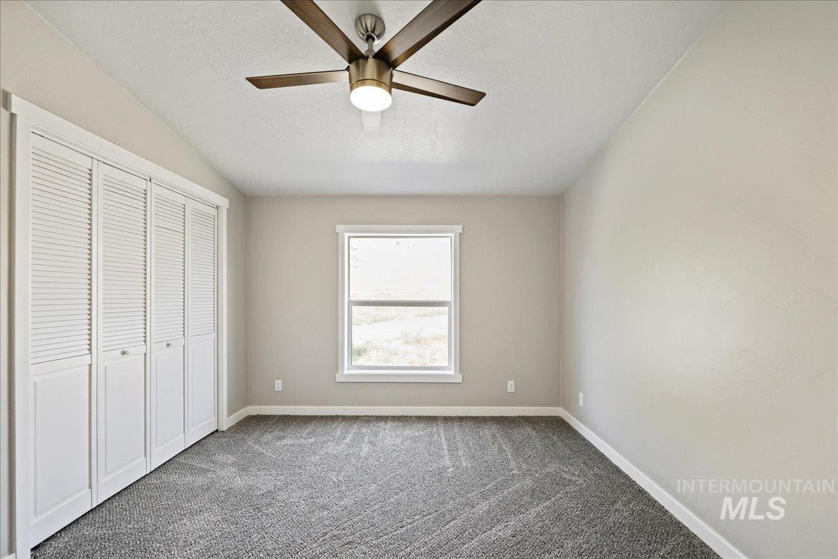 Unfurnished bedroom featuring dark colored carpet, a closet, ceiling fan, and a textured ceiling