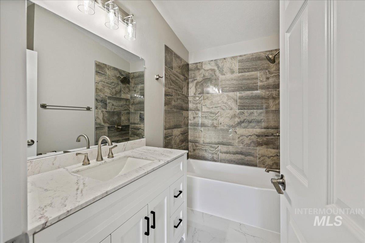 Full bath featuring  shower combination, vanity, and light marble finish floors