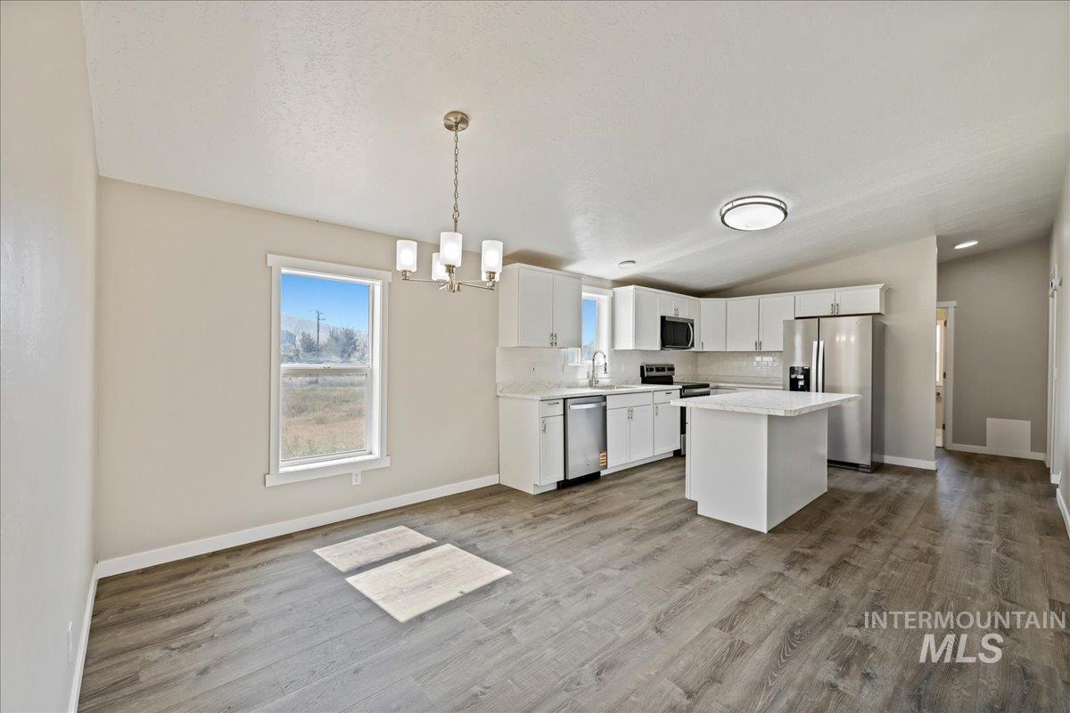Kitchen with a center island, appliances with stainless steel finishes, tasteful backsplash, white cabinets, and pendant lighting