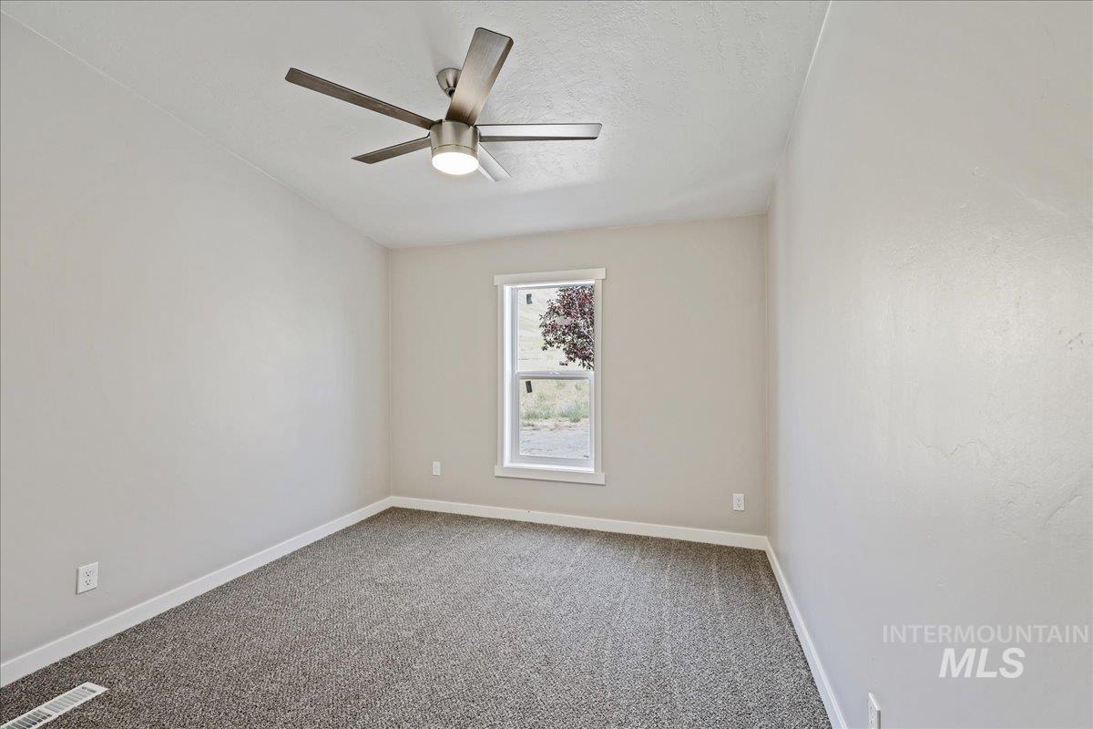 Empty room featuring carpet, a ceiling fan, and a textured ceiling