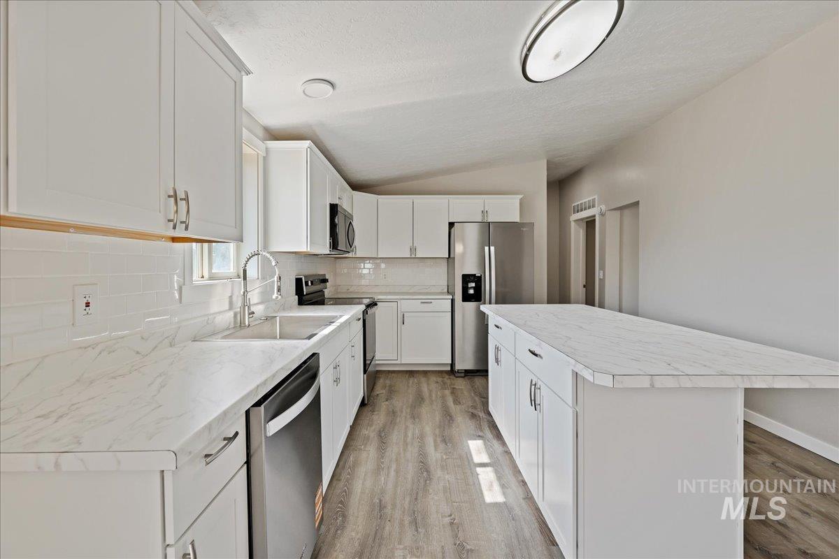Kitchen featuring light countertops, decorative backsplash, appliances with stainless steel finishes, light wood finished floors, and vaulted ceiling