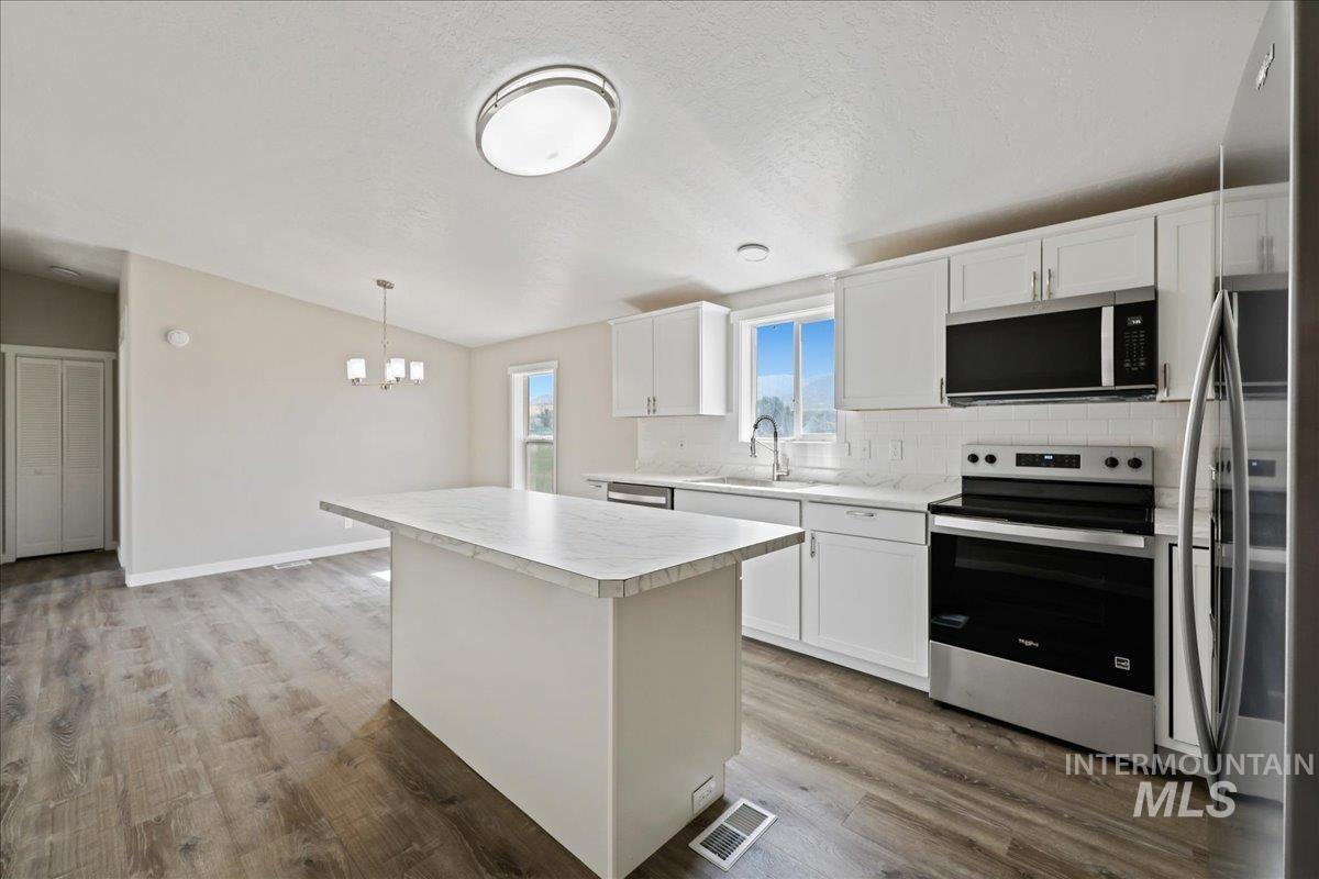 Kitchen with stainless steel appliances, light countertops, backsplash, white cabinetry, and lofted ceiling
