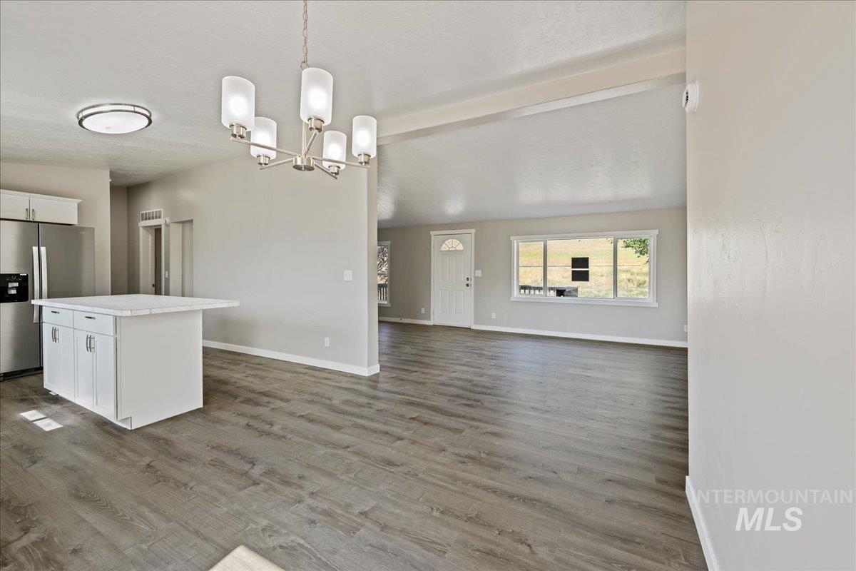 Kitchen featuring white cabinets, stainless steel refrigerator with ice dispenser, decorative light fixtures, open floor plan, and light wood-style floors