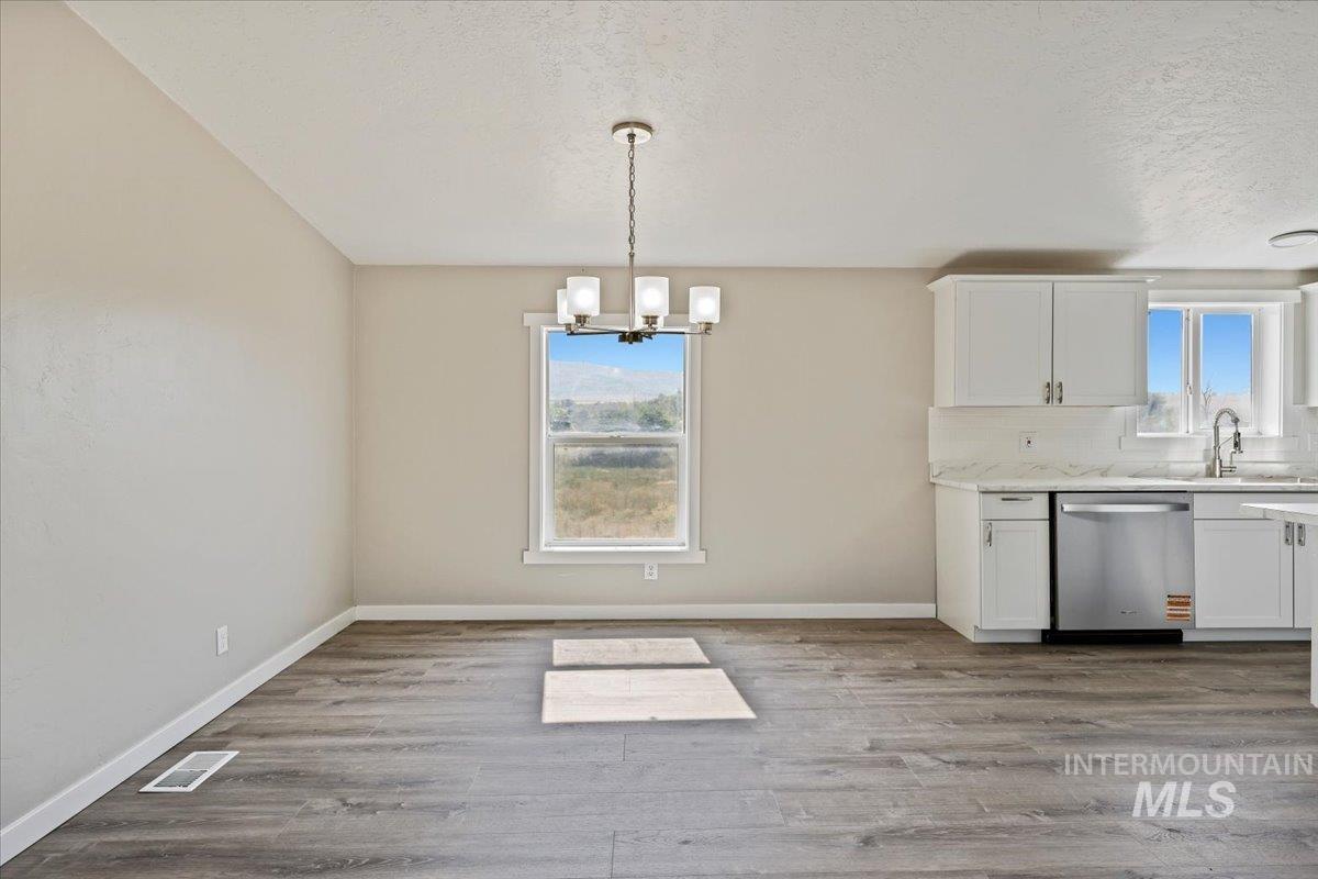 Unfurnished dining area with a chandelier, light wood-type flooring, and a textured ceiling