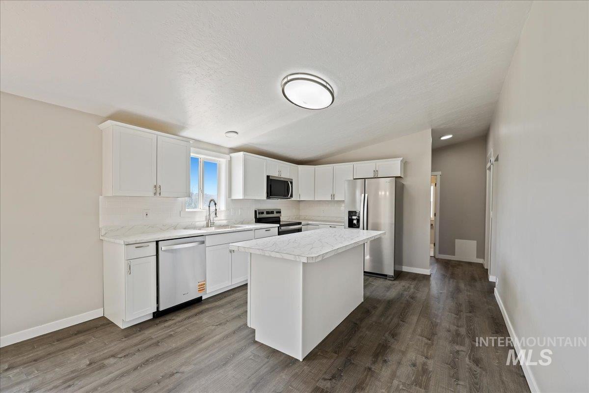 Kitchen with white cabinetry, light countertops, stainless steel appliances, lofted ceiling, and decorative backsplash
