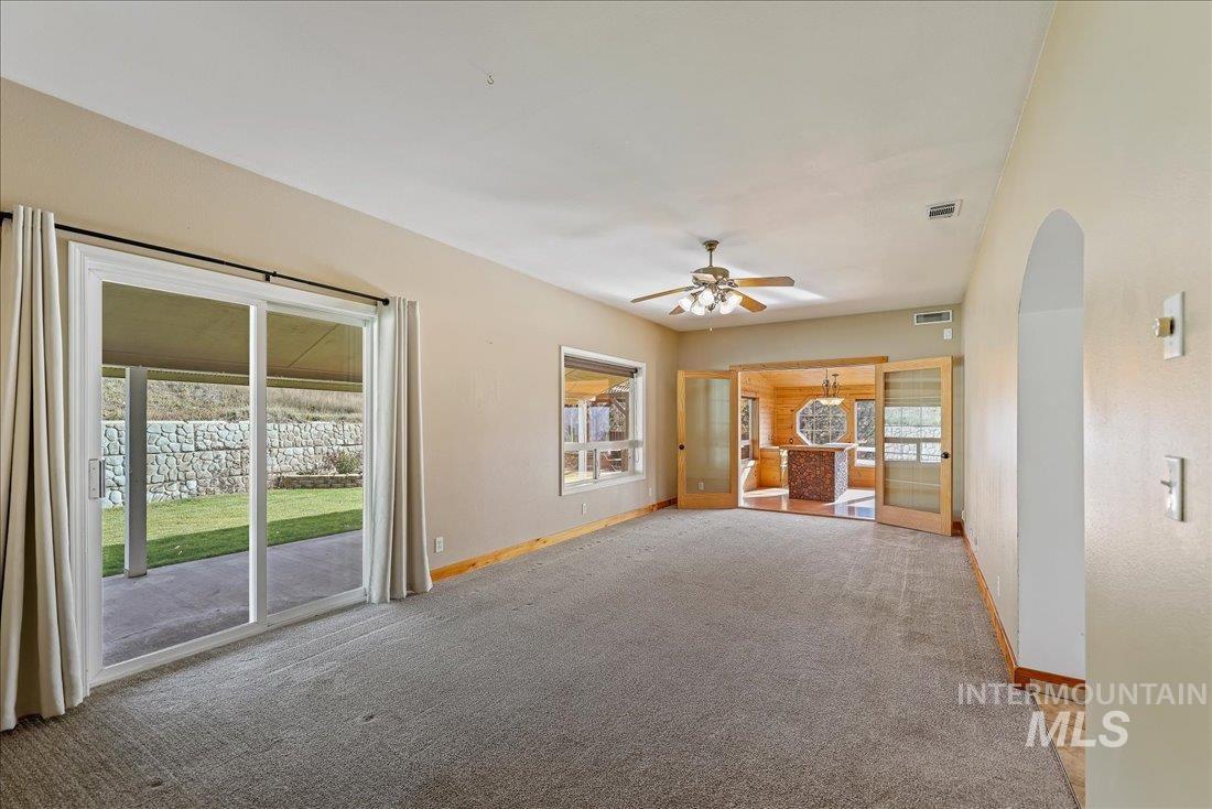 Unfurnished living room featuring carpet, arched walkways, and ceiling fan