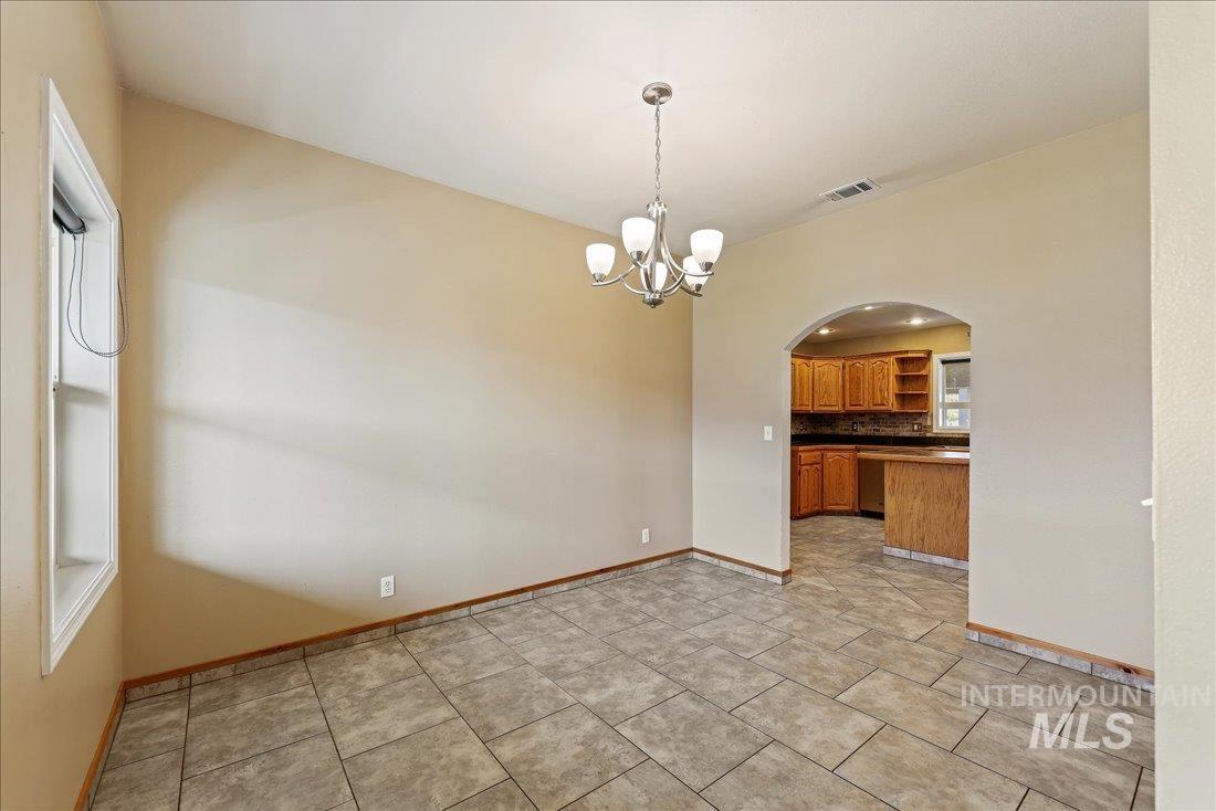 Unfurnished room with arched walkways, a chandelier, and light tile patterned flooring