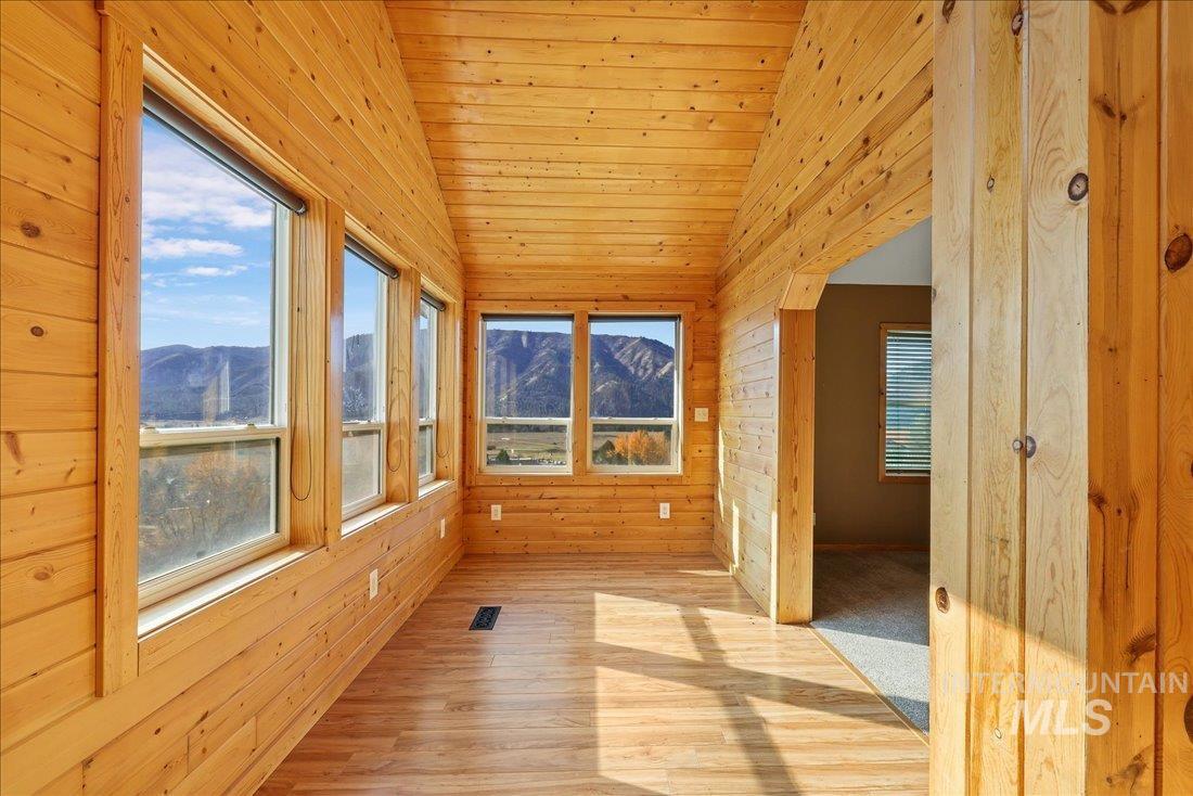 Unfurnished sunroom with lofted ceiling, a mountain view, wood walls, and wood finished floors