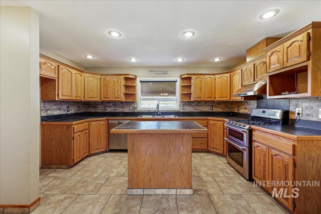 Kitchen featuring open shelves, stainless steel appliances, brown cabinetry, decorative backsplash, and under cabinet range hood