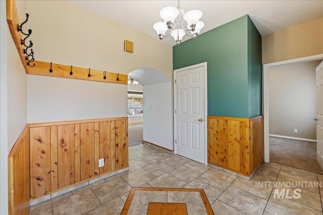 Unfurnished dining area with wood walls, wainscoting, light tile patterned floors, arched walkways, and a chandelier