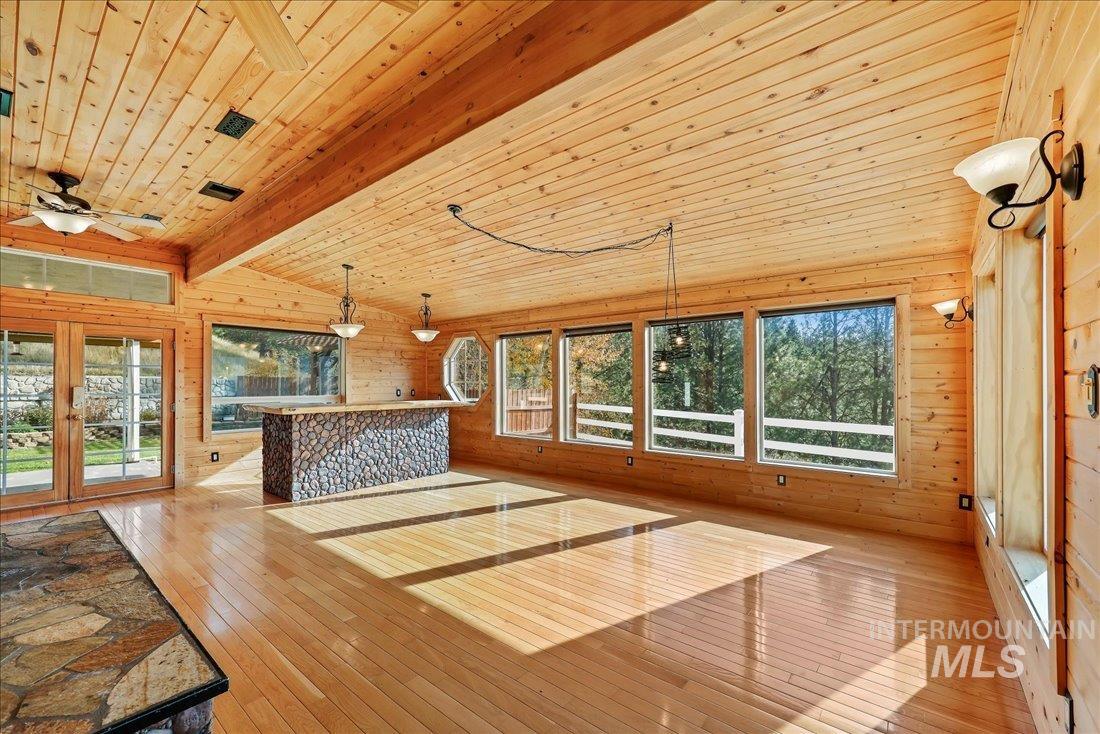 Unfurnished living room with wooden walls, wood-type flooring, wooden ceiling, a dry bar, and french doors