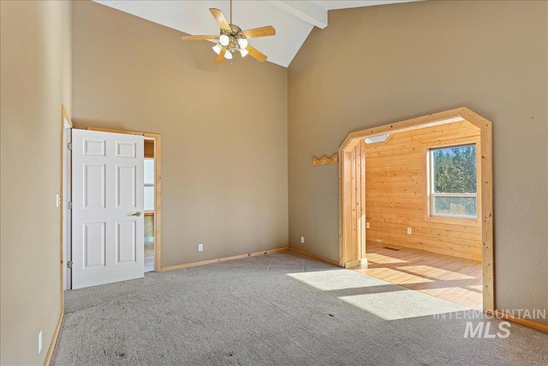 Carpeted spare room featuring high vaulted ceiling, beam ceiling, ceiling fan, and wood walls