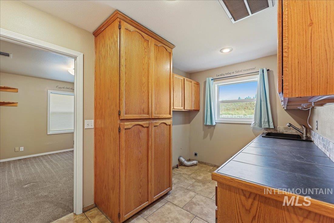 Laundry area featuring electric dryer hookup, light tile patterned floors, cabinet space, and recessed lighting
