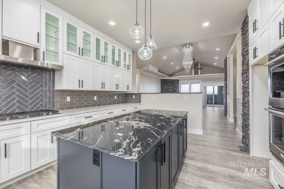 Kitchen featuring dark stone countertops, a kitchen island, lofted ceiling, white cabinets, and pendant lighting