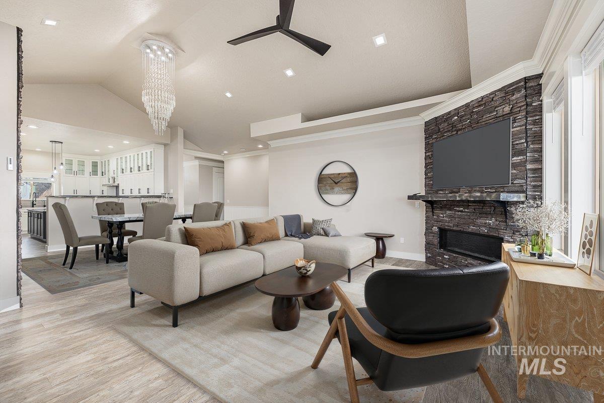 Living area with a large fireplace, vaulted ceiling, light wood-type flooring, a ceiling fan, and a chandelier