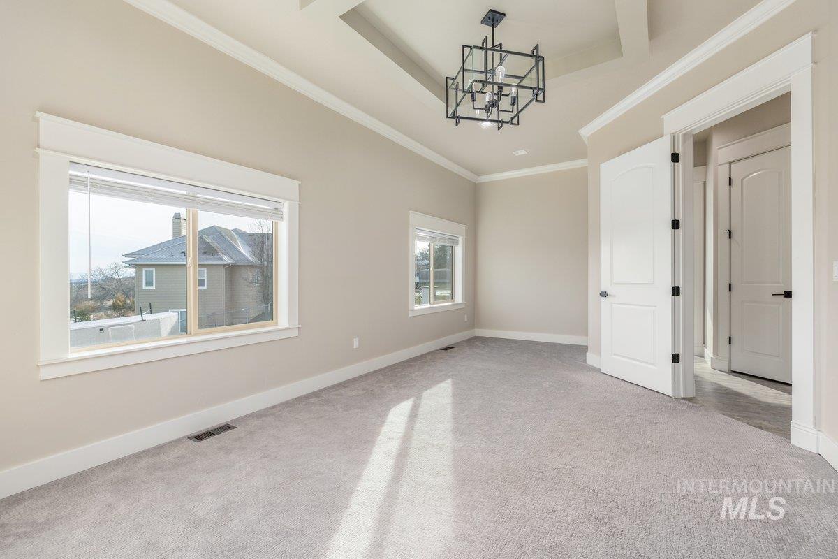 Carpeted empty room featuring a chandelier, crown molding, and a raised ceiling