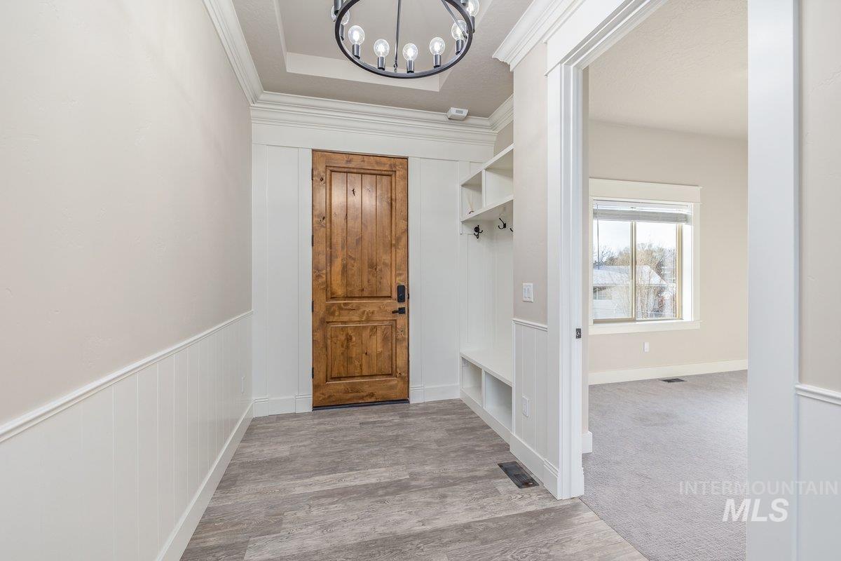 Entrance foyer with a chandelier, light wood finished floors, ornamental molding, and a raised ceiling