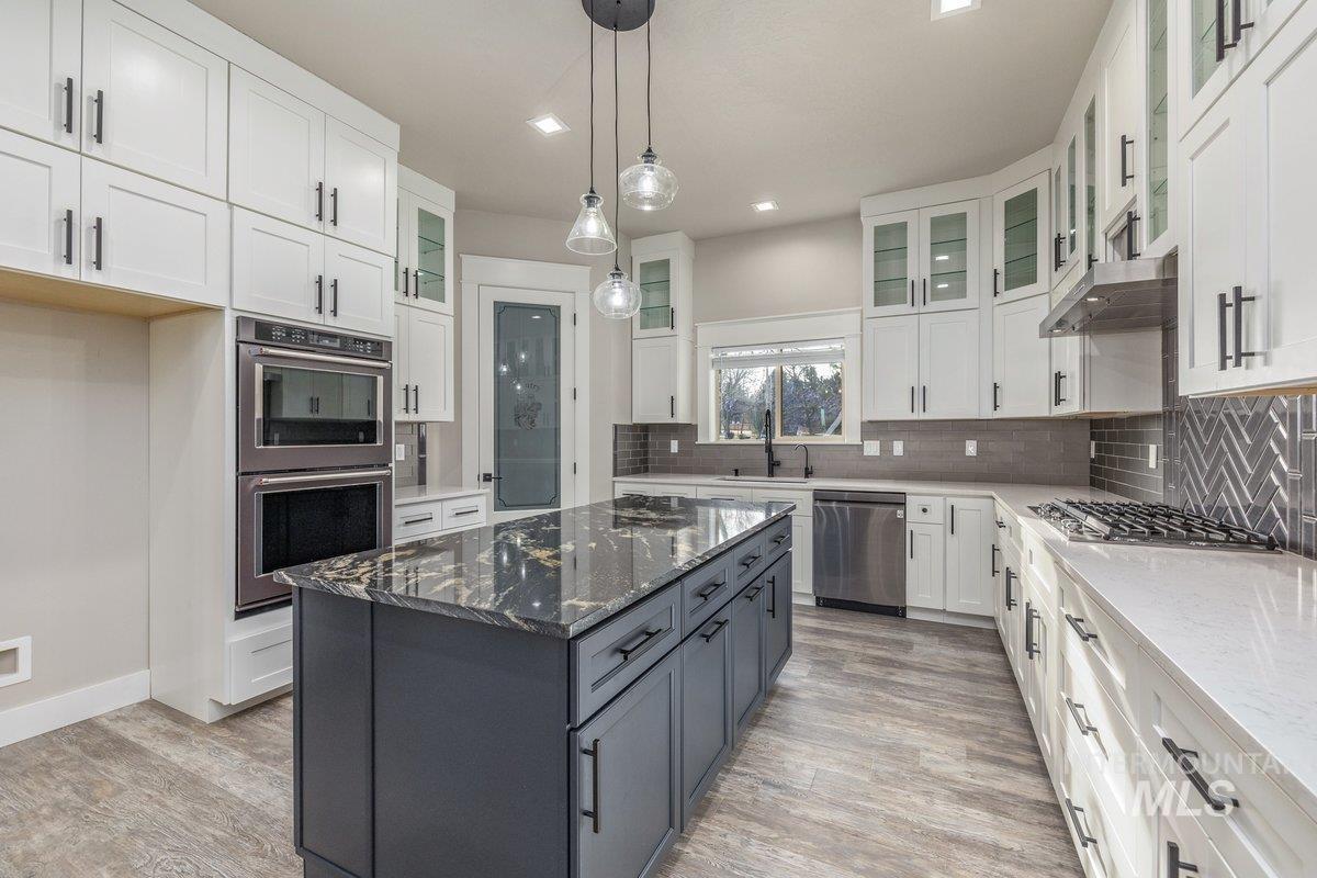 Kitchen featuring dark stone counters, hanging light fixtures, glass insert cabinets, a kitchen island, and white cabinets