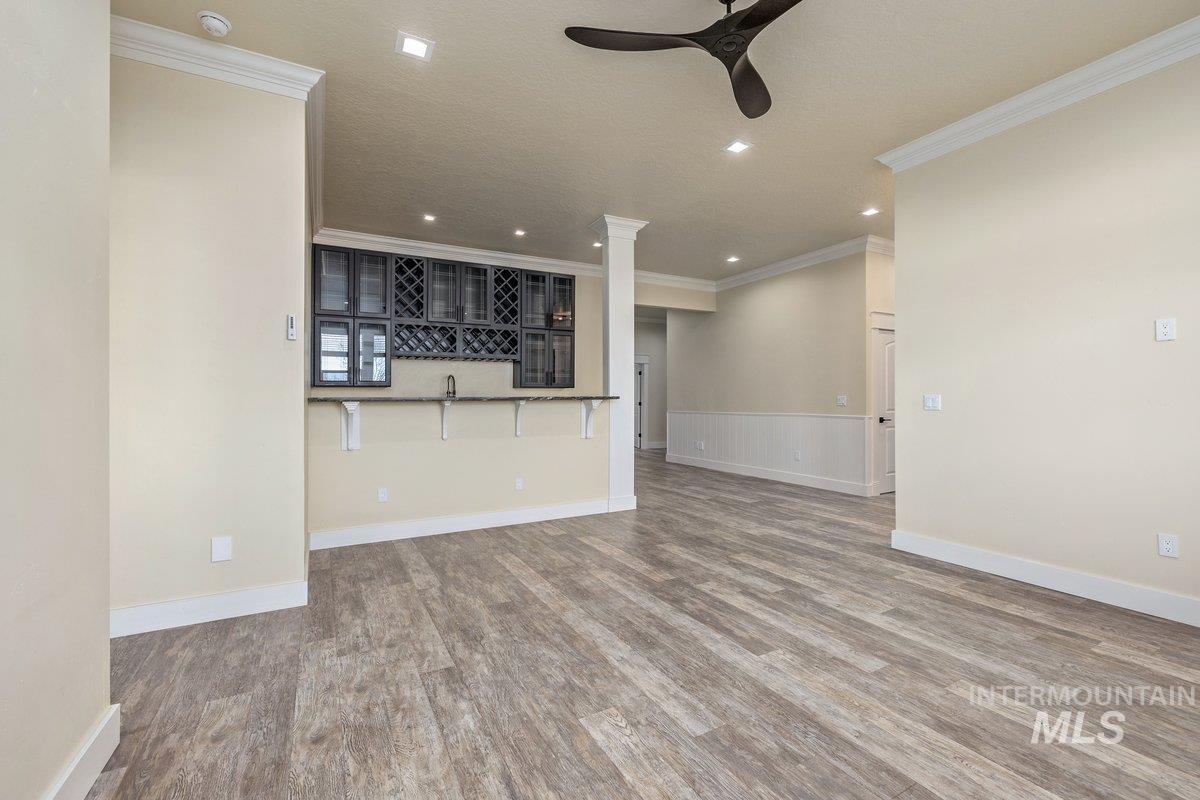 Unfurnished living room featuring wood finished floors, crown molding, ceiling fan, recessed lighting, and a wainscoted wall