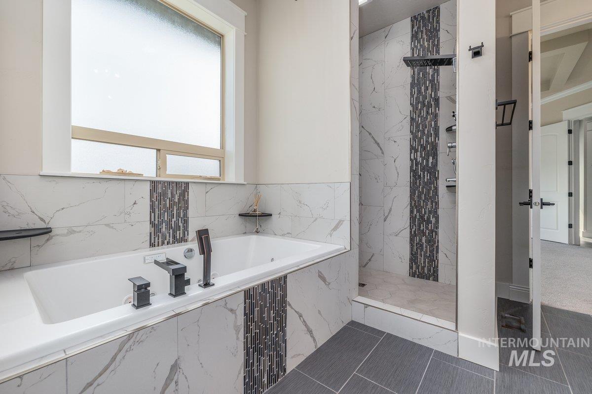 Full bathroom featuring a garden tub, a marble finish shower, and dark tile patterned floors