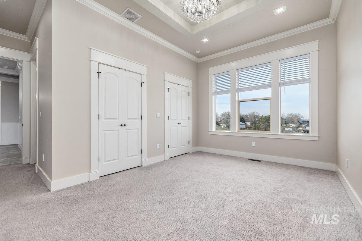 Unfurnished bedroom with two closets, ornamental molding, light carpet, and a chandelier