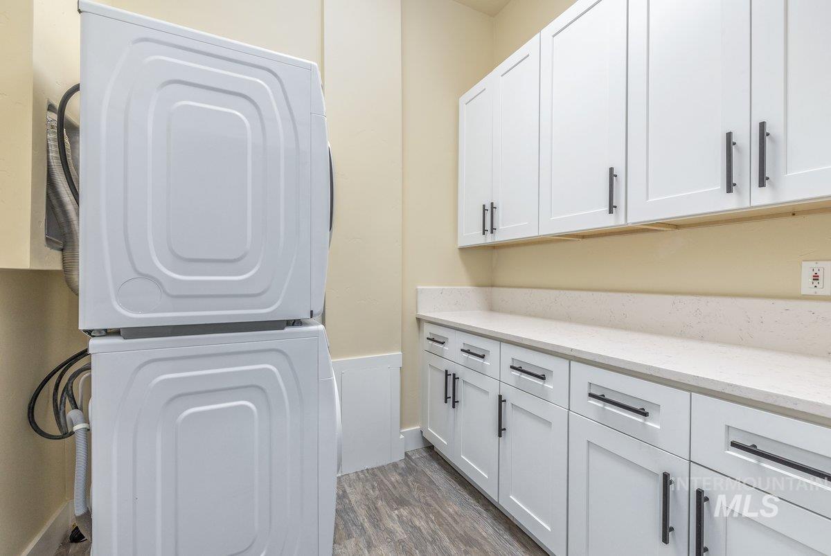 Laundry area with estacked washer and dryer, dark wood-type flooring, and cabinet space