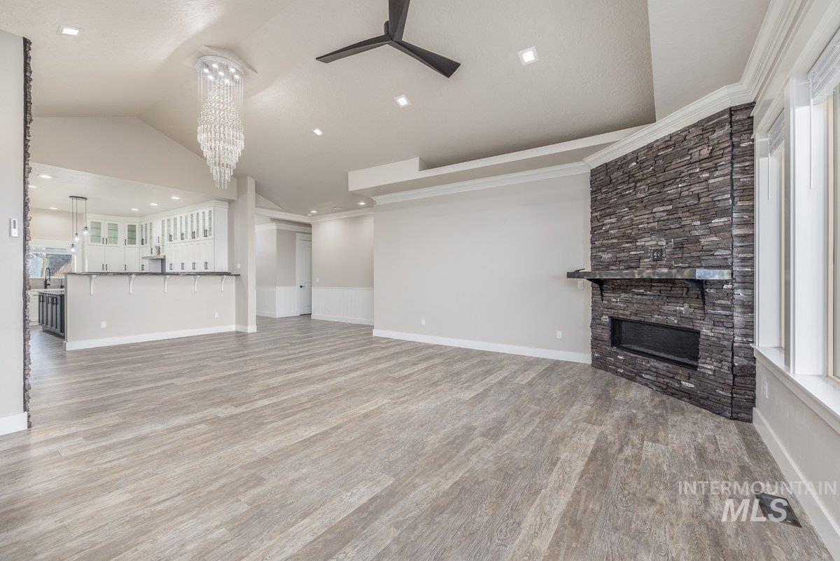 Unfurnished living room featuring a stone fireplace, light wood finished floors, a chandelier, lofted ceiling, and a ceiling fan